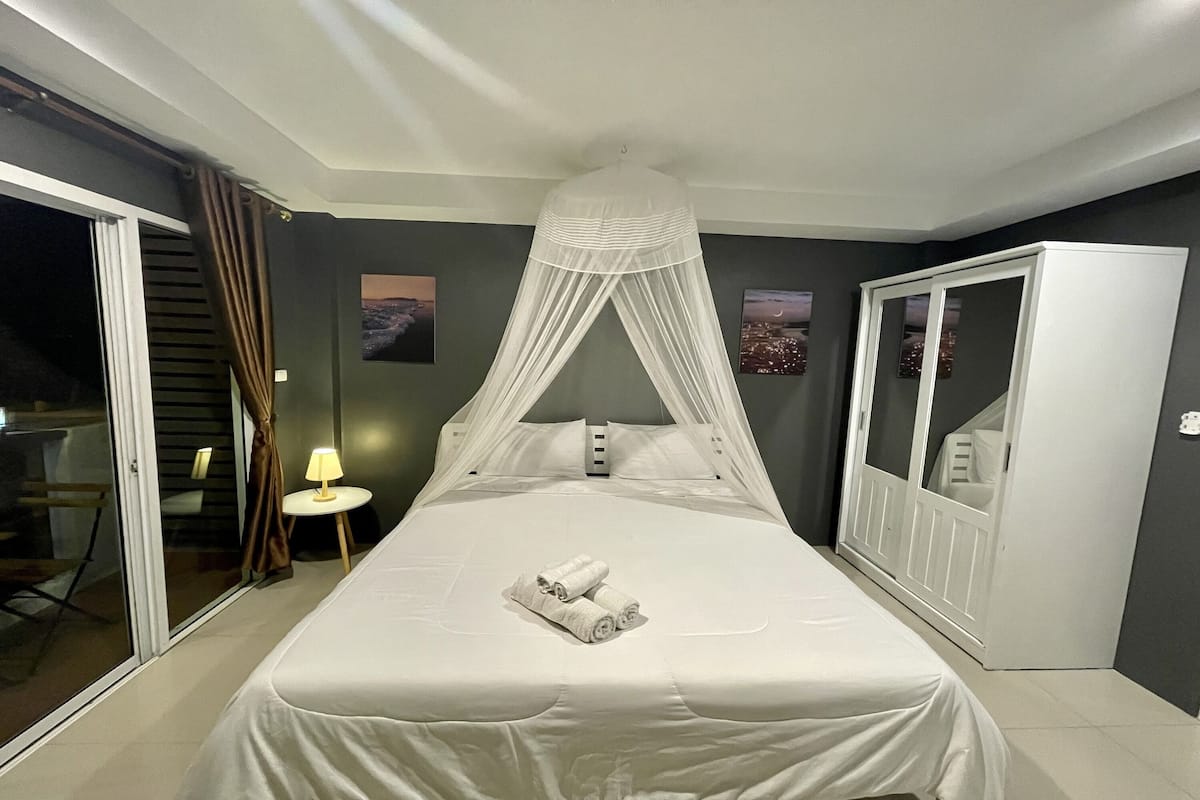 A neatly made bed with a canopy, a bedside lamp, and a set of towels.