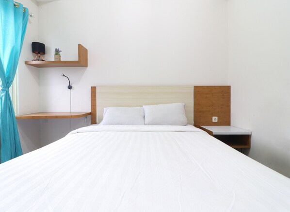 A neatly arranged hotel room with a large bed, a bedside table, a nightstand, and a small shelf with a lamp and a plant.