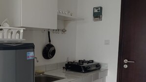 Una cocina compacta con refrigerador, estufa, una olla colgada y un pequeño estante sobre el lavamanos.
