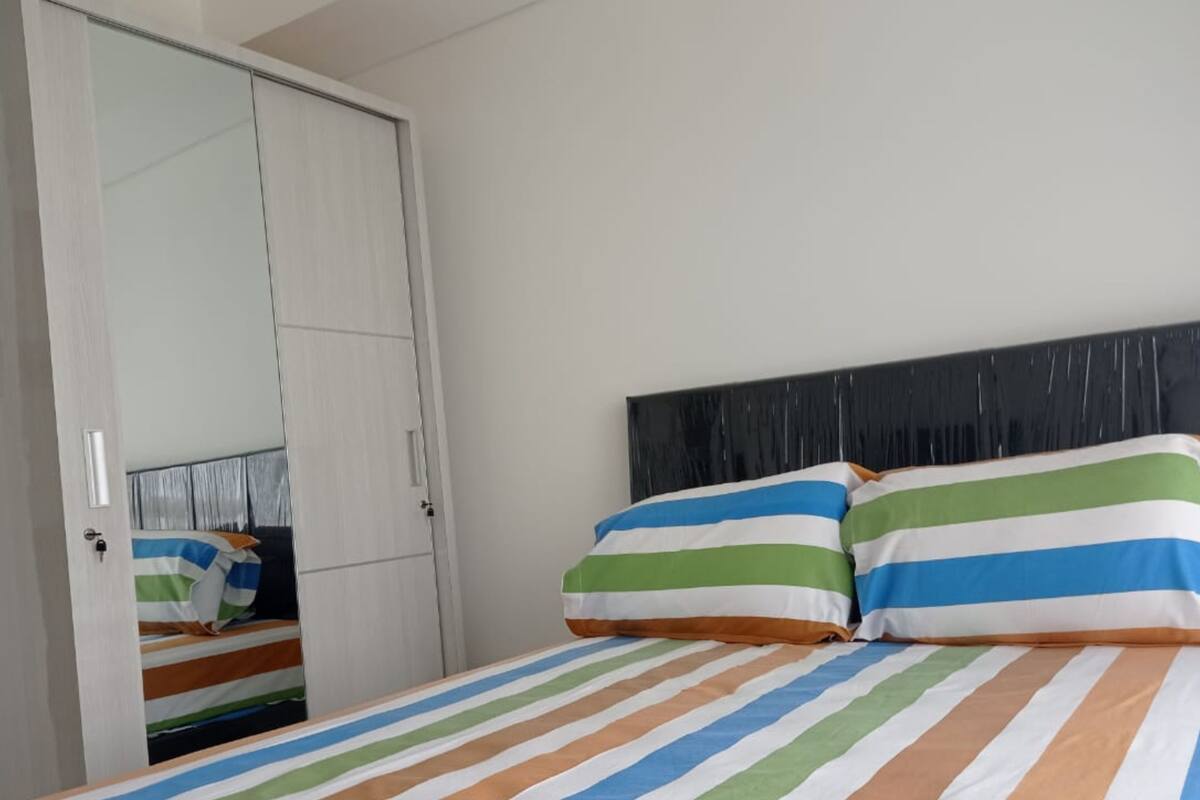 Un dormitorio con colcha a rayas, cabecero negro y armario blanco con espejo.