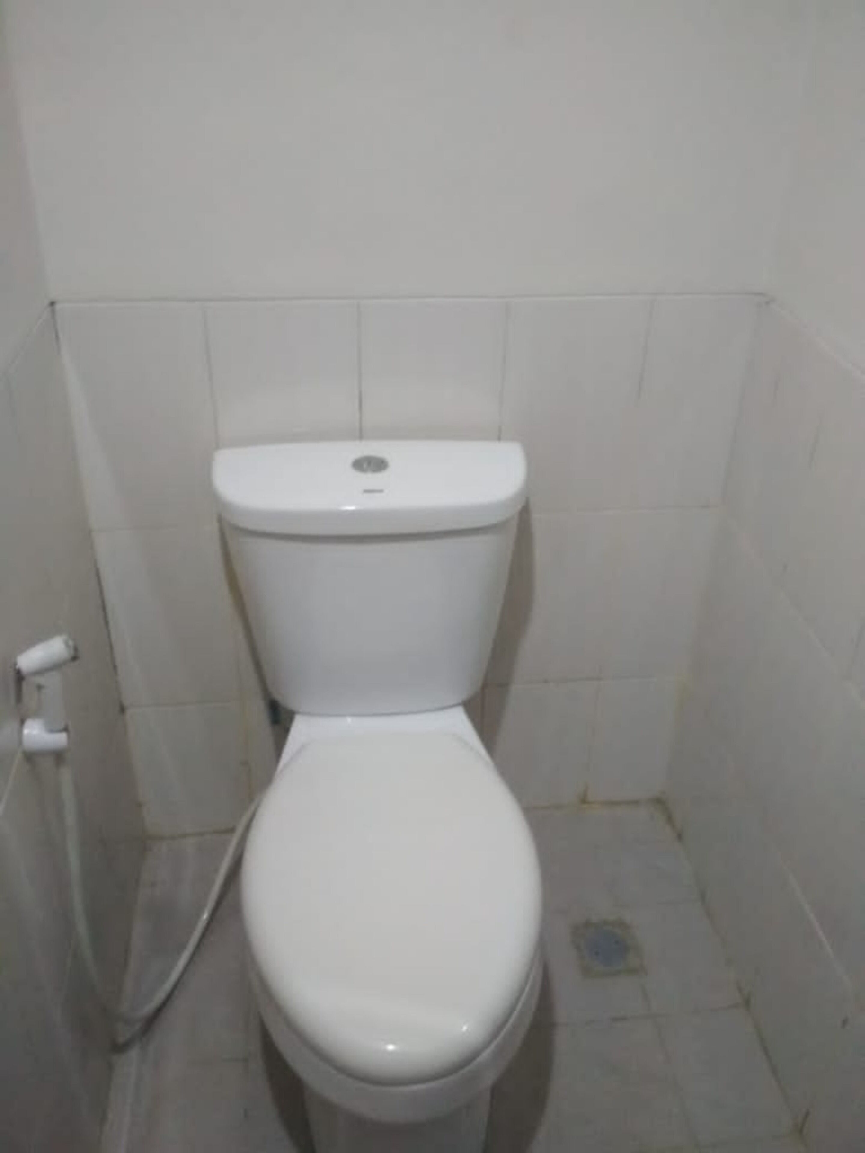 Eine weiße Standardtoilette in einem kleinen, gefliesten Badezimmer mit einer schlichten weißen Wand.