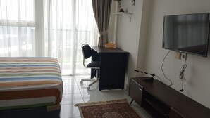 Una habitación de hotel con cama, escritorio, silla, televisión y una pequeña estantería.