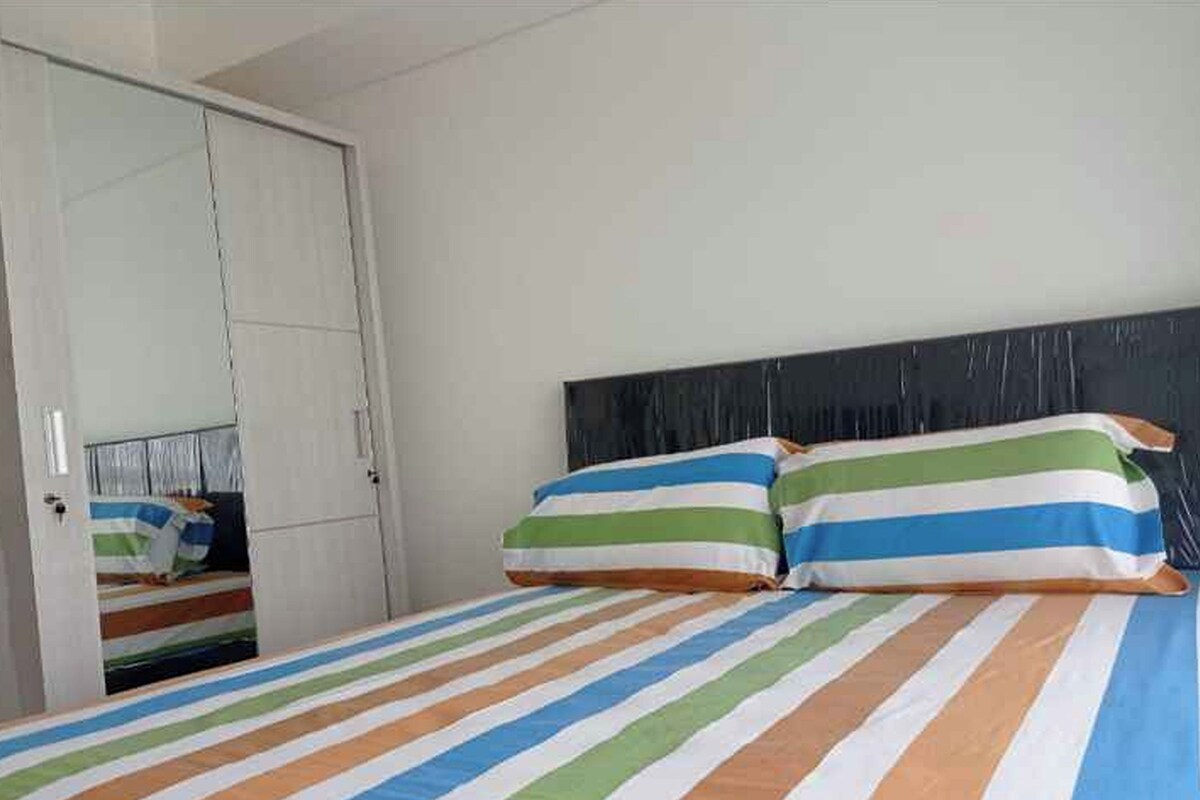 A bedroom with a bed, striped bedding, a wardrobe, and a mirror.
