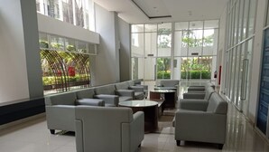 A spacious lobby with a seating area featuring sofas and a coffee table, large windows offering views of greenery, and a clean, modern design. - Sultan Premiere Casa De Parco (Pagedangan)