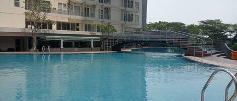 Una piscina con un puente, rodeada por un edificio con varios balcones y una zona cubierta.