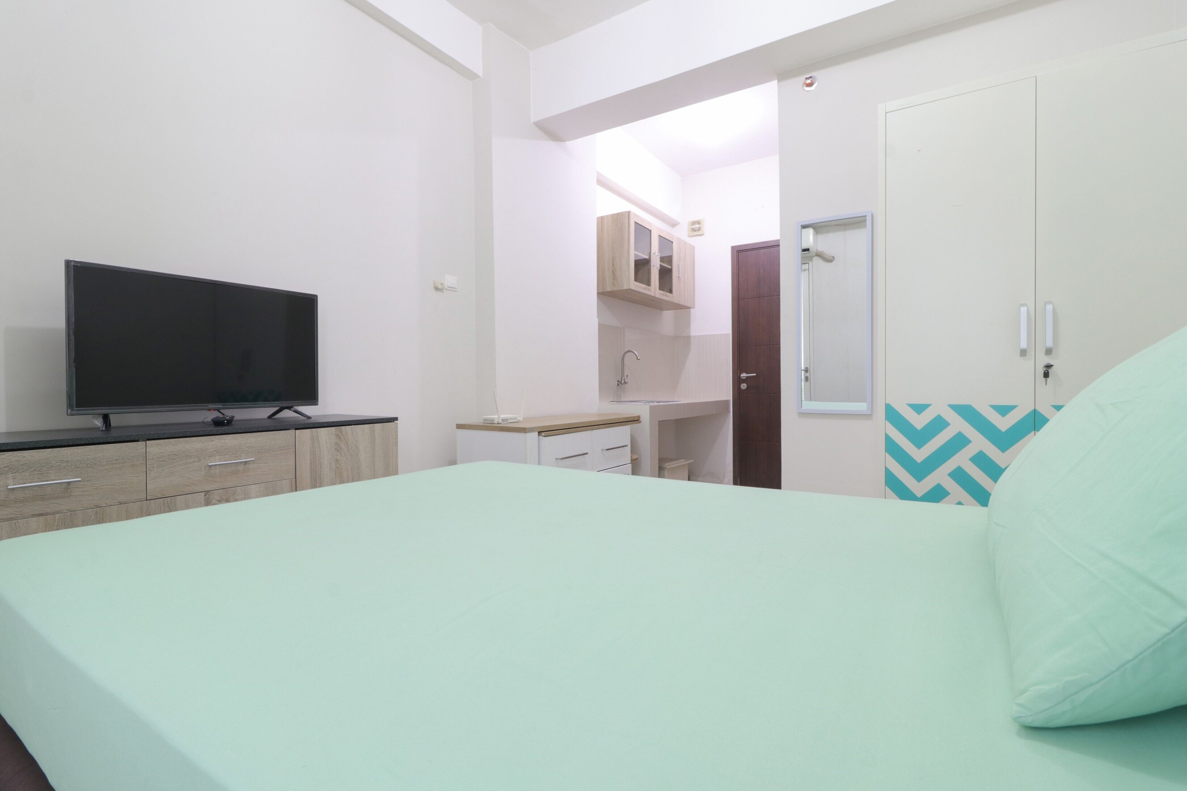 Un dormitorio con cama, televisor, armario y un baño visible a través de una puerta abierta.