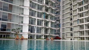 A modern building with a swimming pool, lounge chairs, and a red umbrella. - Sultan Premiere HI (South Tangerang)