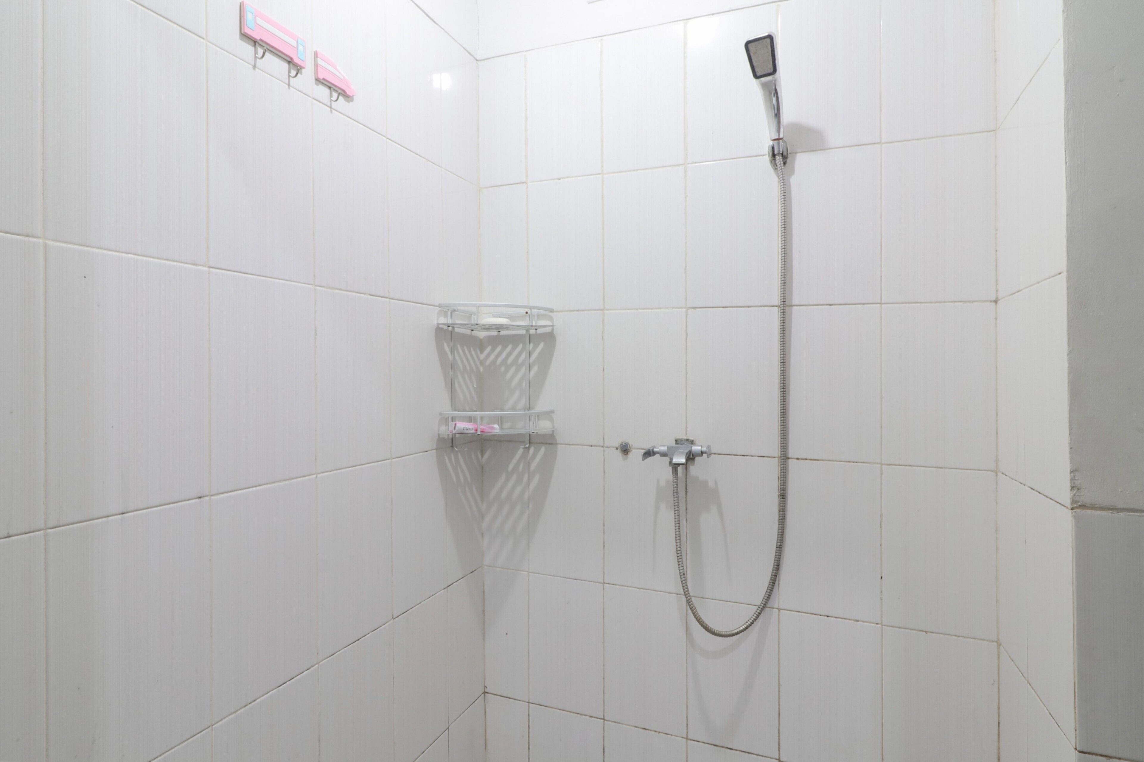 A small, white-tiled bathroom with a shower, a toilet, and a soap dispenser.