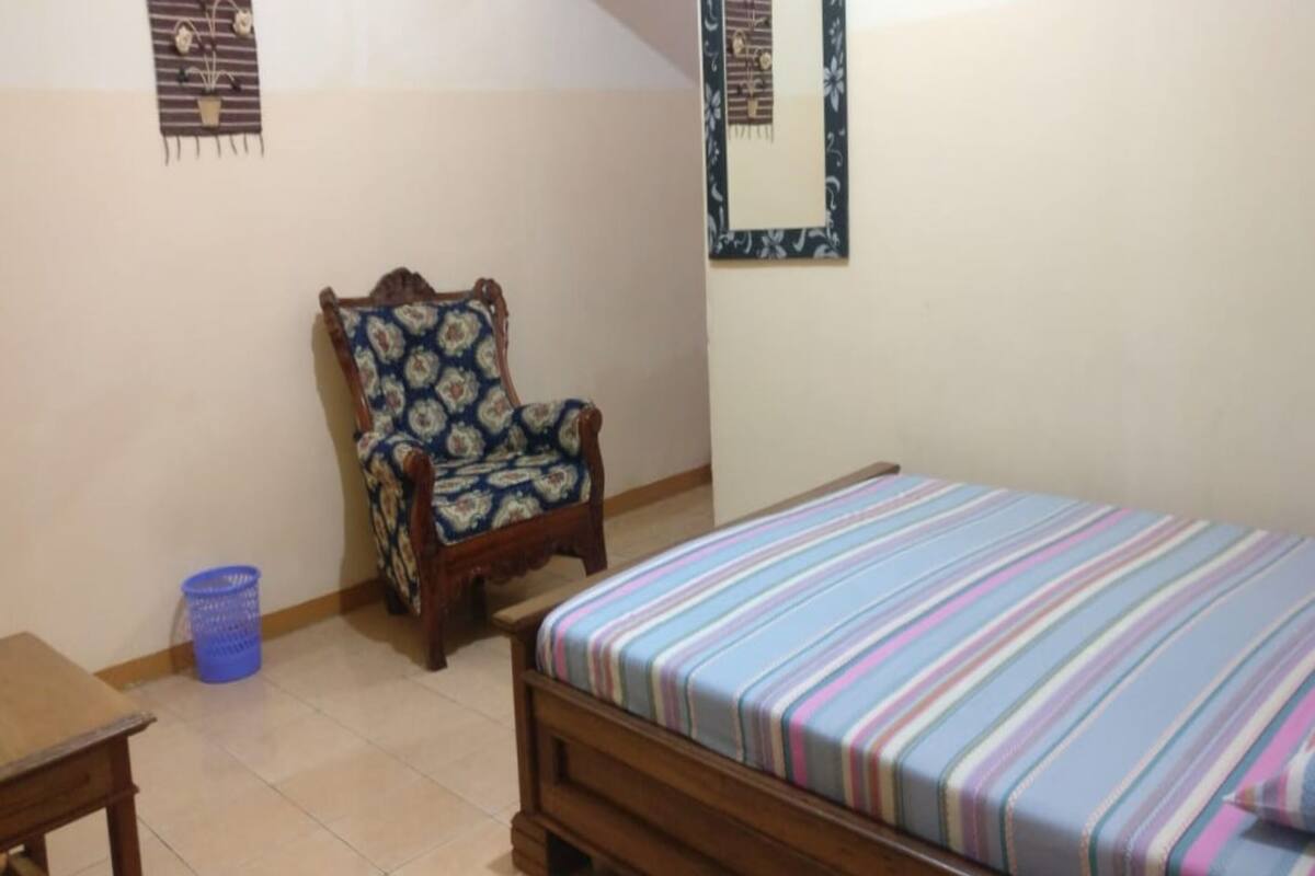 Ein Schlafzimmer mit einem hölzernen Bett, einem Sessel, einem kleinen Tisch und einem blauen Korb.