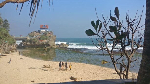 A beach with a rocky outcrop, a bridge, and a clear view of the ocean. - Winahyu Family Resort (Wonosari)