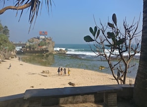 Una playa con un promontorio rocoso, un puente y una vista despejada del océano.