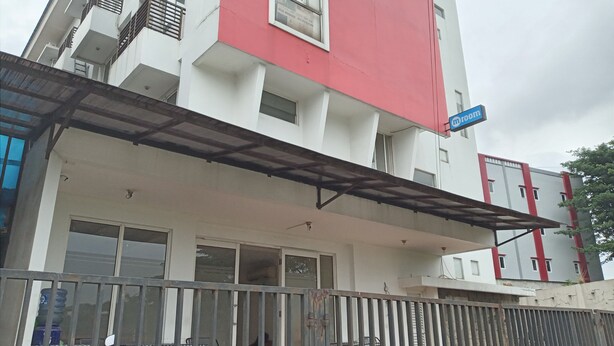 Un edificio a più piani con facciata rossa e bianca, una zona esterna coperta con tavolo e sedie, e un cartello che indica una stanza.