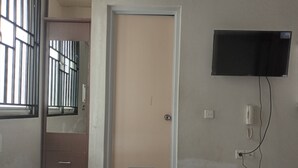 Una camera d'albergo con un letto, una televisione a parete, una porta e una finestra con sbarre.