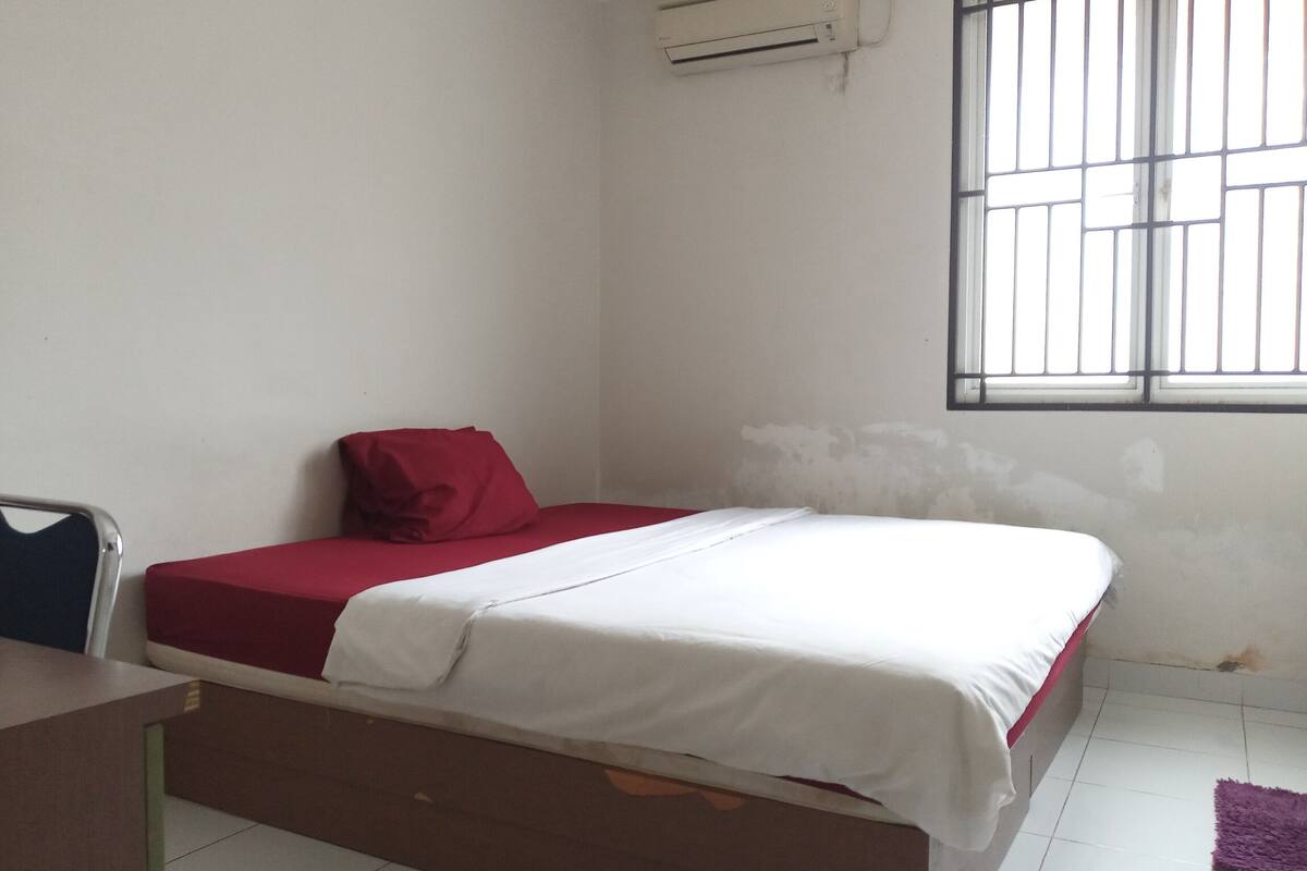 A small, clean room with a single bed, a desk, and a window with bars.