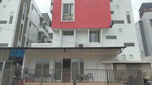 Un edificio a più piani con una sezione rossa al piano superiore, un ingresso con cancello e una zona relax esterna coperta con tavoli e sedie.