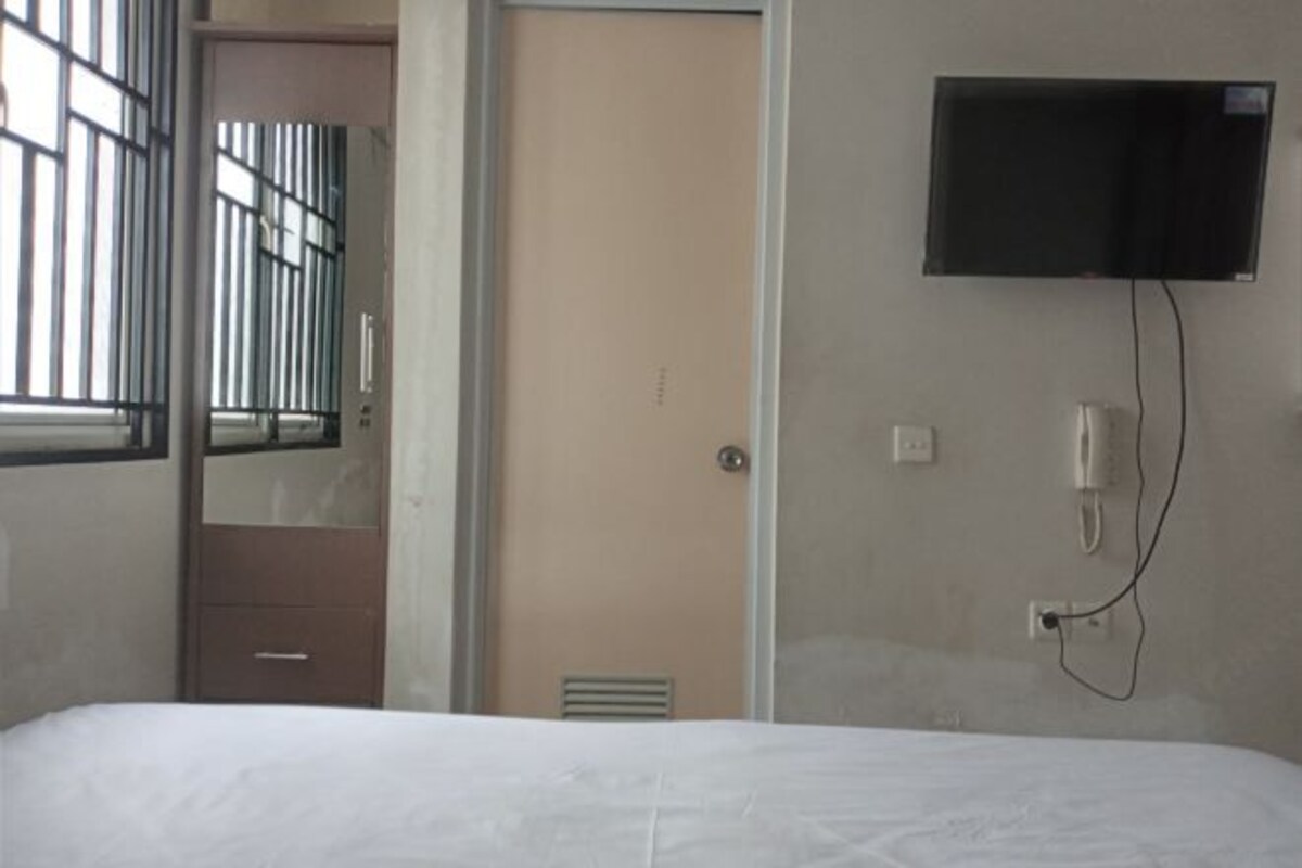 A hotel room with a bed, a television mounted on the wall, a door, and a window with bars.