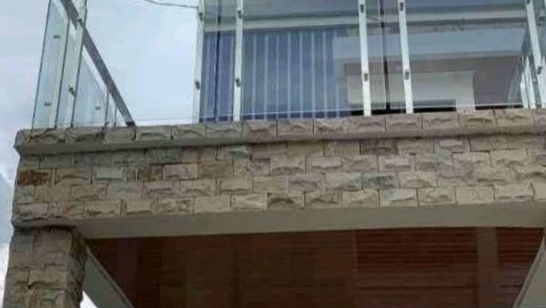 Un edificio de dos pisos con fachada de piedra y un balcón con barandilla de vidrio.