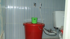 Un baño con un balde rojo, un recipiente verde y un inodoro.