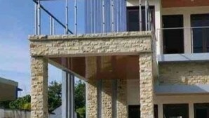 Un edificio de dos pisos con fachada de piedra y un balcón en el nivel superior.