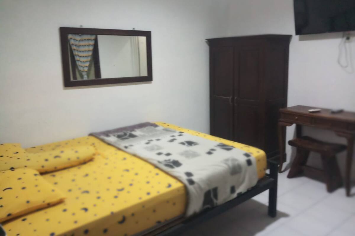 A small room with a single bed, a wooden desk, a wardrobe, and a mirror on the wall.