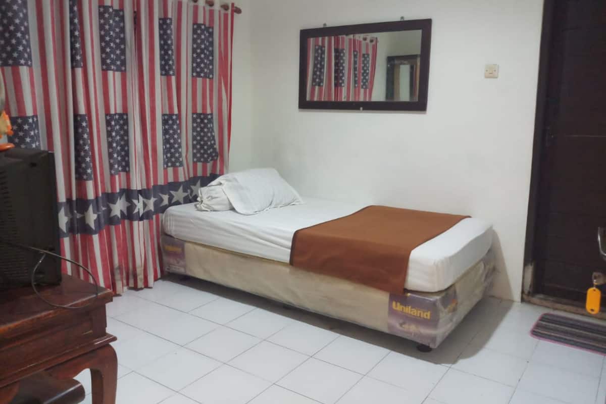 A single-bed room with a mattress labeled "Uniland," a wooden desk, a television, and curtains with an American flag pattern.