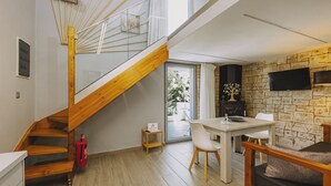 A modern interior with a wooden staircase, a dining area, and a stone wall. - Mini Bella Gonia (Rethymno)