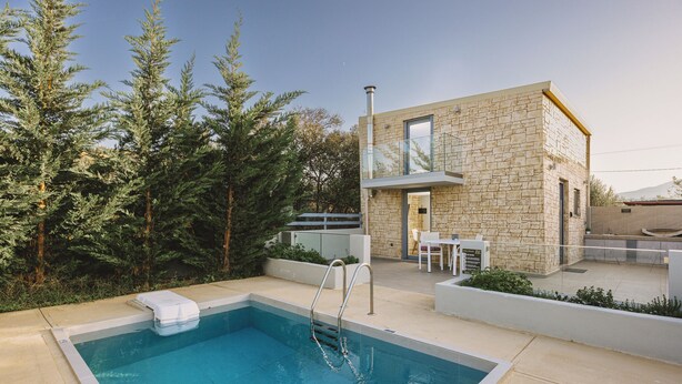 A modern pool area with a stone building, outdoor furniture, and surrounding trees. - Mini Bella Gonia (Rethymno)