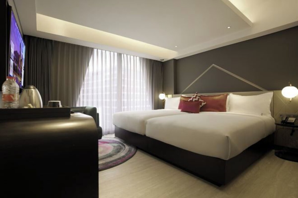 Une chambre d’hôtel moderne, dotée d’un grand lit, d’une télévision et d’un bureau avec une lampe.
