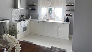 A modern kitchen with white cabinets, a gas stove, a sink, and a window with sheer curtains. - Magnolia Home Lucca Campagna (Capannori)
