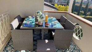 A balcony with a table set for breakfast, wicker furniture, and a view of the garden. - Magnolia Home Lucca Campagna (Capannori)