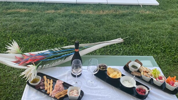 A poolside setup with a table offering a variety of snacks and drinks, surrounded by a lush green lawn and a blue pool. - Magnolia Home Lucca Campagna (Capannori)