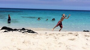 Eine Strandansicht mit klarem türkisblauem Wasser, Menschen beim Schwimmen und Spielen sowie einem sandigen Ufer.