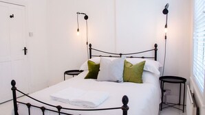 Una cama con estructura metálica, dos mesitas de noche y una lámpara fijada a la pared.
