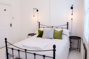 A bed with a metal frame, two bedside tables, and a wall-mounted light fixture. - Charming Boutique House – Stylish Stay Just Minutes from Margate Beach (Kent)