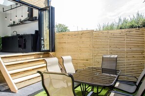 An outdoor patio with a dining table and chairs, a grill, and a kitchen area with a window. - Charming Boutique House – Stylish Stay Just Minutes from Margate Beach (Kent)