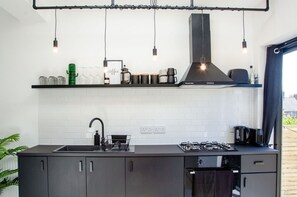A modern kitchen with a gas stove, black cabinets, a black countertop, and a hanging light fixture. - Charming Boutique House – Stylish Stay Just Minutes from Margate Beach (Kent)