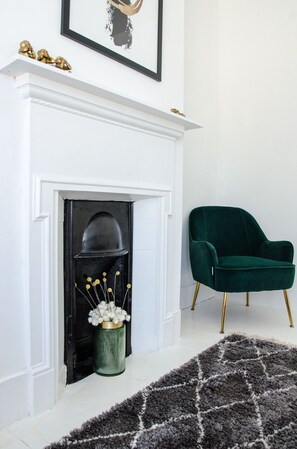 A room with a white fireplace, a green chair, and a patterned rug.