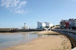 A coastal area with a sandy beach, a modern building, and a lighthouse. - Charming Boutique House – Stylish Stay Just Minutes from Margate Beach (Kent)
