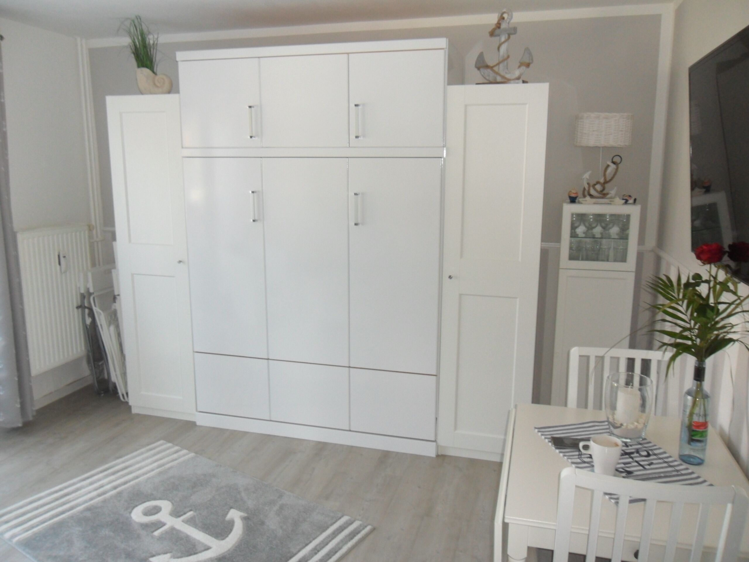 A room with a white wardrobe, a dining table with a vase and a bottle, and a radiator.
