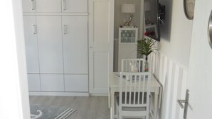 A kitchen with white cabinets, a dining table with chairs, a potted plant, and a TV mounted on the wall.