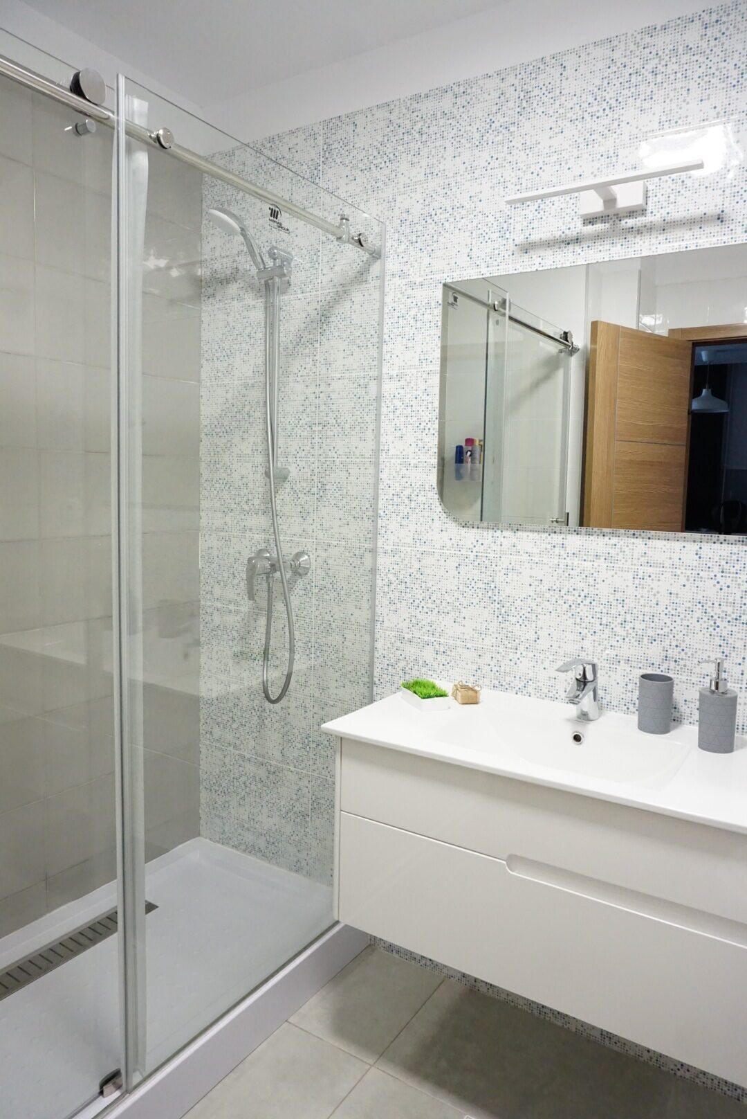 Un baño moderno con ducha envuelta en vidrio, tocador blanco con espejo y salpicadero de azulejos.