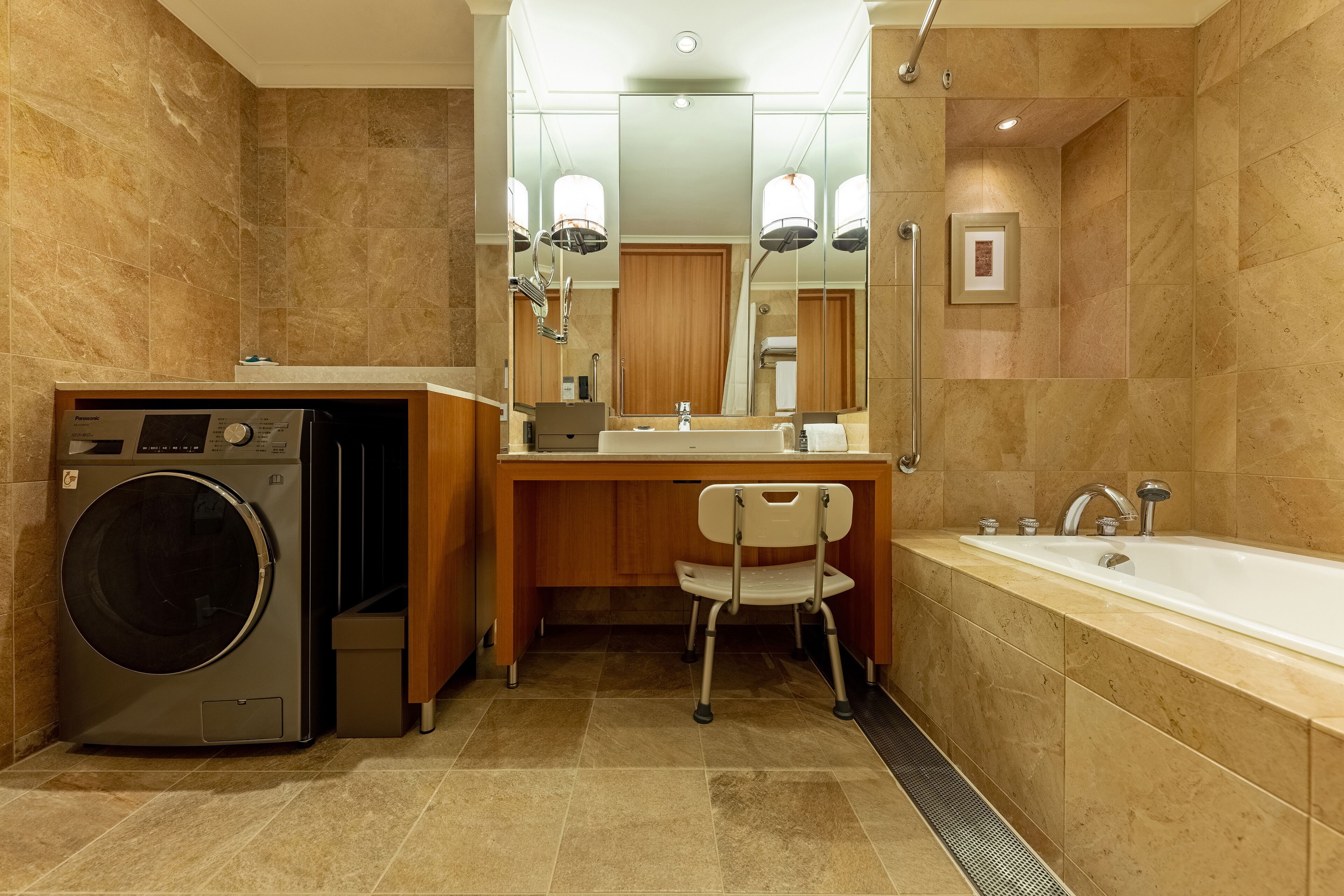 A modern bathroom with a built-in washer, a vanity with a mirror, a chair, and a bathtub.