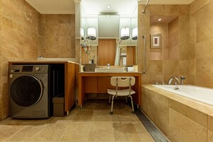 A modern bathroom with a built-in washer, a vanity with a mirror, a chair, and a bathtub.