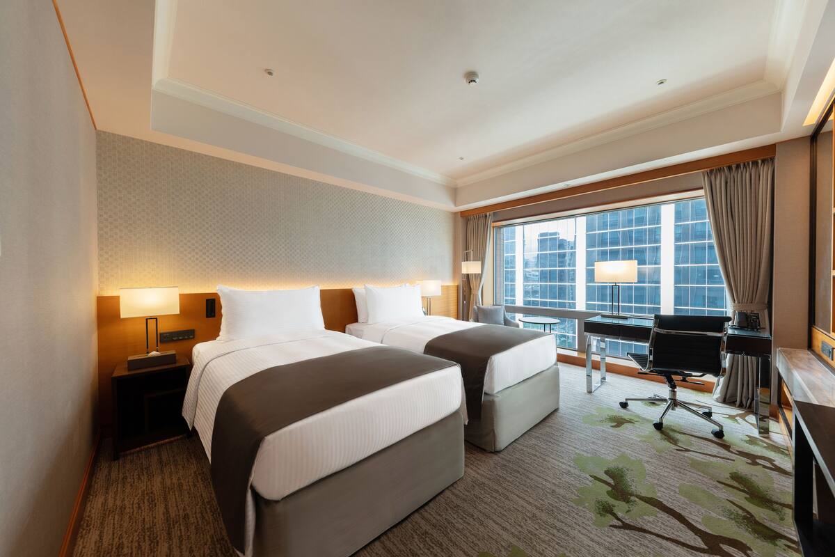 A hotel room with two beds, a desk, a chair, and a large window with curtains.