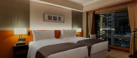 A hotel room with two beds, a nightstand, a lamp, a window with curtains, and a city view.