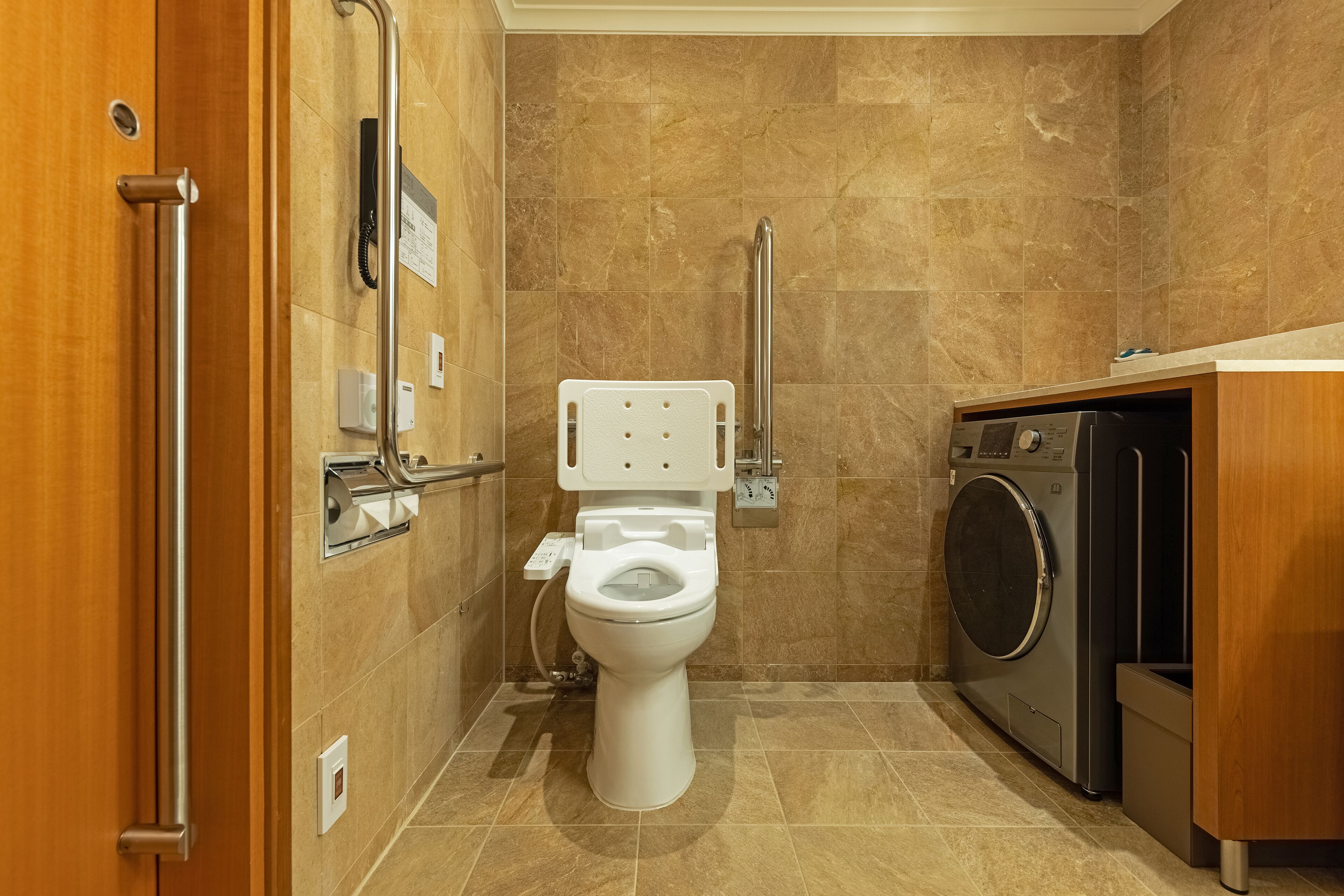 A compact bathroom with a toilet, handrail, and a washing machine.