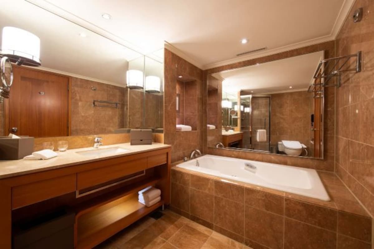 Une salle de bain moderne dotée d’un grand miroir, de deux vasques, d’une baignoire et d’un meuble-lavabo avec des étagères.