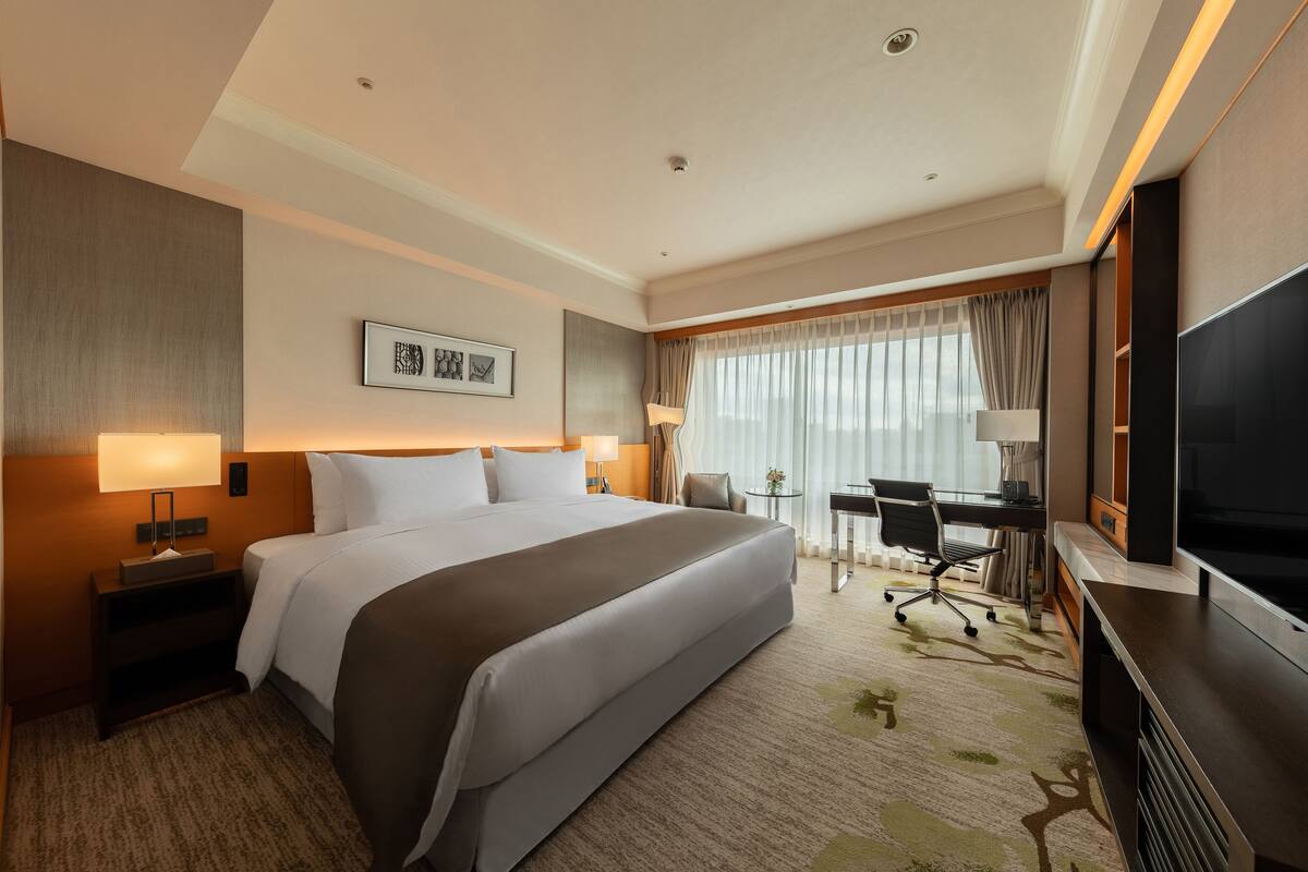 A hotel room with a large bed, a desk with a chair, a television, and a window with curtains.