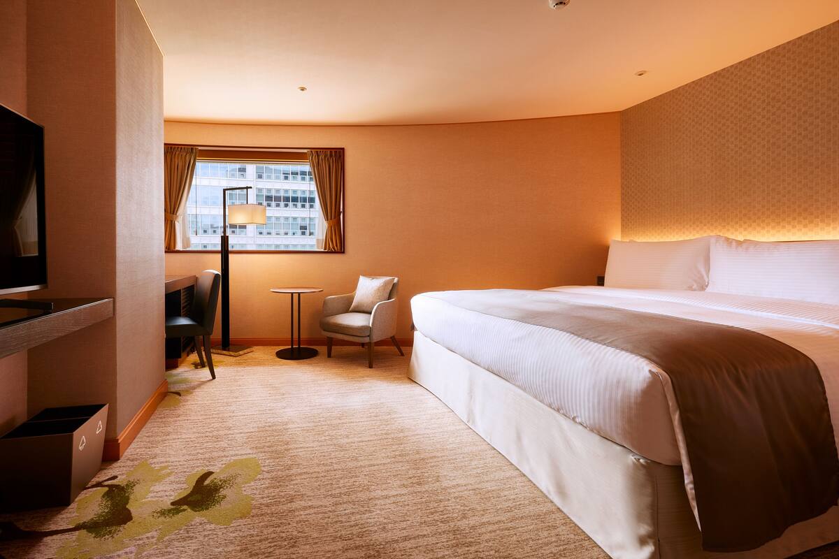A hotel room with a large bed, a desk, a chair, and a window with curtains.