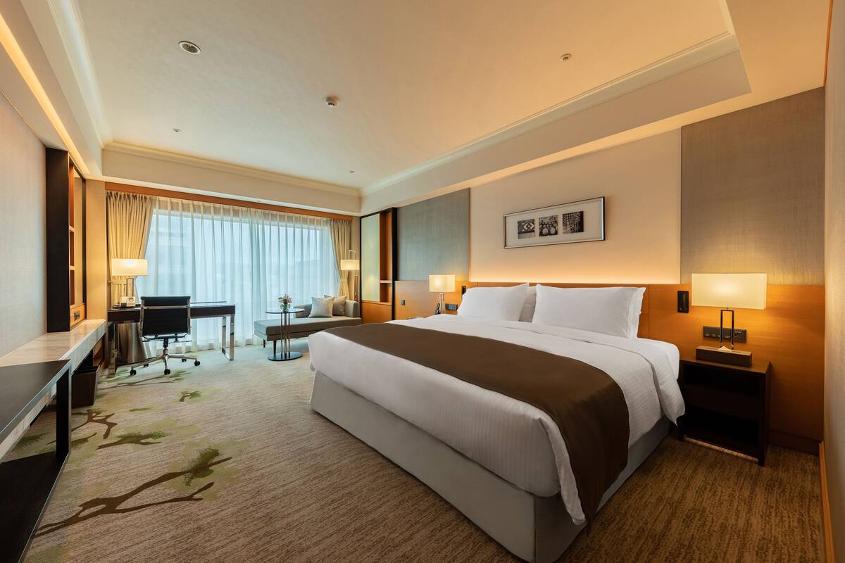 A hotel room with a large bed, a desk, a chair, and a small table.